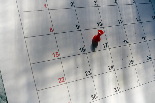 Close up of a red pushpin pinned on a paper monthly calendar with eyeglasses, concept for event reminder, schedule planning, appointment tracking, and deadline management