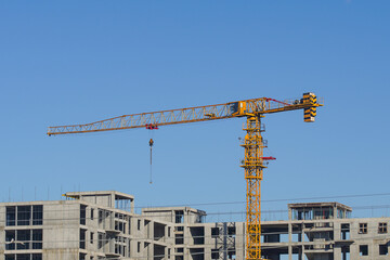 Construction process of building from monolithic frame of reinforced concrete panels using orange tower-type crane against background clear blue sky in city © Po
