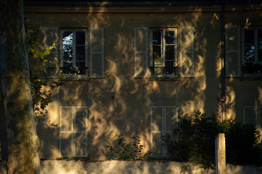 Crescent shadow projections from a partial solar eclipse appear on a building facade in Paris, France. Sunlight passing through tree leaves forms natural pinhole images.