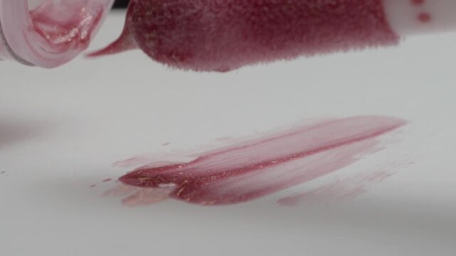 Macro view of a lip gloss applicator applying pink cosmetic gloss, highlighting the soft doe foot tip, smooth texture and precise makeup application with selective focus.