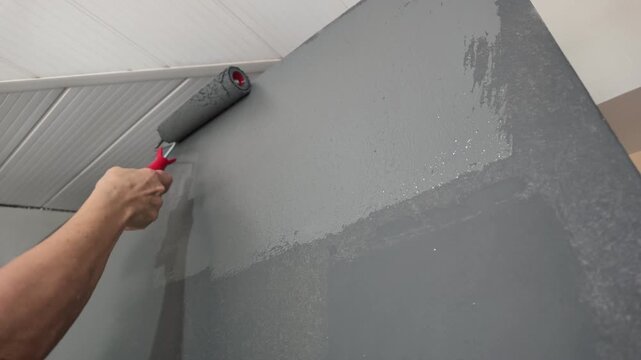 Close up of female hands applying gray paint with a roller during an interior home renovation project.