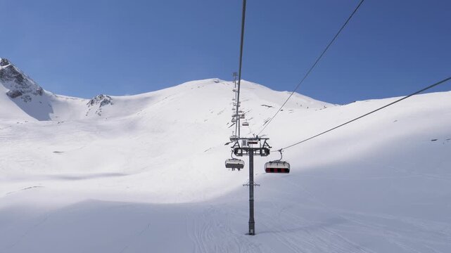 Pov from chairlift ascending sunlit snow covered mountain at ski resort. The ski lift pylon passes by, offering a scenic view of the pristine alpine landscape