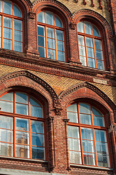 Architectural detail of historic red brick building with arched windows and decorative masonry elements in Budapest Hungary street view during sunny day
