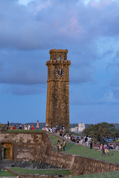 Galle, Southern Province, Sri Lanka - 01 May 2026: View of the historic Galle Dutch Fort clock tower standing tall against a twilight sky, with visitors walking along the grassy ramparts.