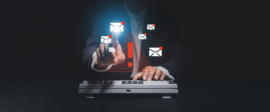 Hand selecting a digital email notification with warning icons above a keyboard. Concept of phishing detection, email security, cyber threats, spam protection, and cybersecurity.
