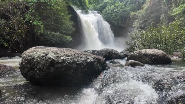 Misty Falls: A majestic waterfall cascades down rocky cliffs, shrouded in mist, with large, moss-covered boulders in the foreground creating a natural, serene landscape.