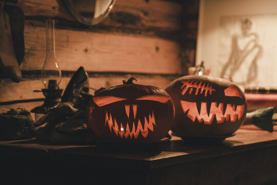 Laane County, Estonia - 31 October 2024: View of two carved jack-o'-lanterns with glowing faces resting on a rustic wooden table in a dimly lit room.
