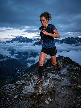 Athletic woman trail running along a rocky mountain ridge above the clouds at dusk, splashing through water, symbolizing endurance, fitness and outdoor adventure in dramatic terrain.