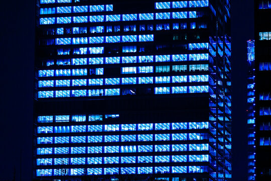 Minimalist front facade view of a modern skyscraper in Tokyo at night with glowing blue office windows.