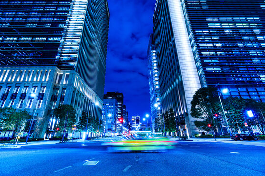 Wide-angle night view of Tokyo financial district skyscrapers with fast-moving traffic light motion blur.