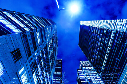 Dramatic low-angle view of illuminated skyscrapers in Tokyo at night under a glowing street lamp and dark sky.