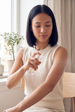 Woman spraying moisturizer on arm in bright bathroom for skincare routine background and body care banner design