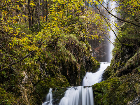 Goriuda waterfall cascades down mossy rocks in a vibrant autumn forest, offering a serene travel destination for nature exploration in the Julian Alps, Chiusaforte, Friuli, Italy, amazing scene.