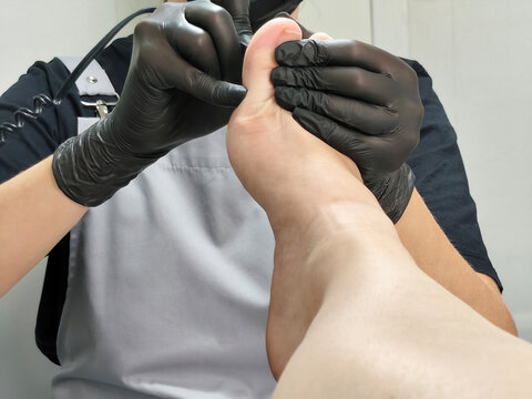 Pedicure procedure with a foot specialist wearing black gloves, close up of toenail care treatment in a beauty salon.
