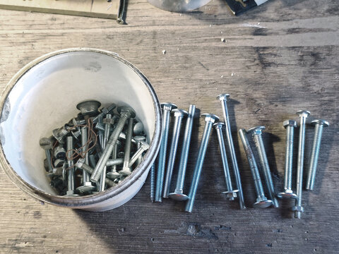 Assorted wood screws and carriage bolts on a wooden workbench in a workshop. Fasteners for construction, carpentry, furniture assembly, DIY home improvement and repair projects.
