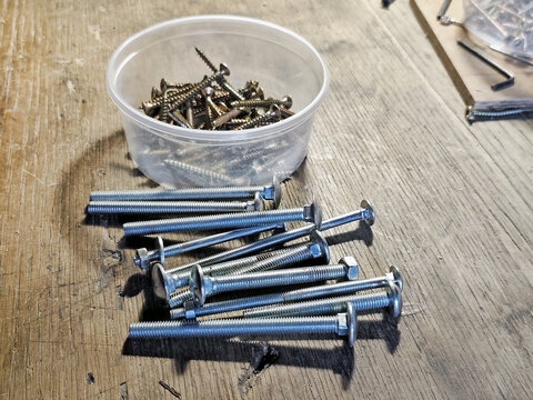Assorted wood screws and carriage bolts on a wooden workbench in a workshop. Fasteners for construction, carpentry, furniture assembly, DIY home improvement and repair projects.

