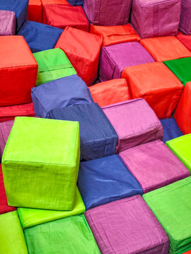 Colorful soft foam cubes stacked together in an indoor children's play area. Bright padded blocks in green, red, blue, and purple colors forming an abstract geometric background. Educational play equi