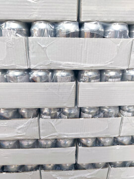 Stacked cardboard boxes filled with aluminum cans wrapped in plastic, arranged in rows for storage or transport, warehouse packaging and bulk distribution concept.
