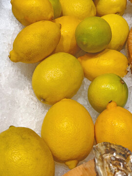 Fresh yellow lemons and a few green citrus fruits displayed on crushed ice at a market, showcasing vibrant colors and natural texture.
