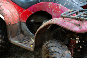 Muddy red all terrain vehicle with dirt splattered fender and knobby tire showing outdoor off road use and rugged texture, conveying adventure and worn utility
