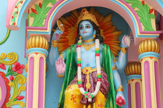 Colorful four-armed Hindu god Vishnu or Narayana statue sculpture on a traditional temple wall decoration.