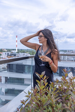 Stylish woman in black dress enjoying wine on a rooftop terrace with city background