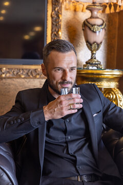Handsome businessman in black suit holding a glass of whiskey in a luxury room