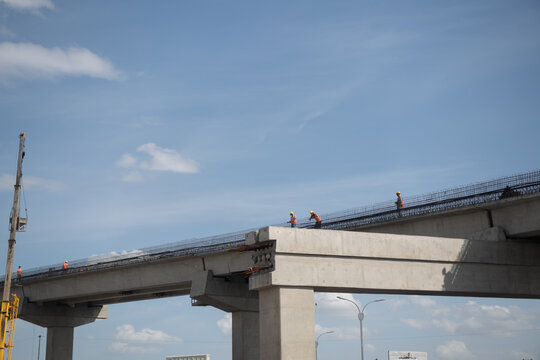 Nairobi, Kenya - 06 February 2022: View of construction workers in orange vests and hard hats working on the concrete structure of an overpass under a blue sky.
