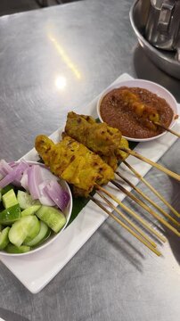 Vertical video showing a hand grabbing a pork satay skewer and dunking it into savory peanut dip. 