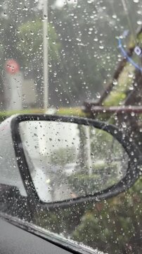 Vertical 4K video showing right side wing mirror covered in raindrops reflecting a line of traffic behind in heavy rain. 