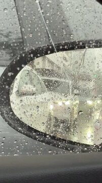 Vertical 4K close up shot of left wing mirror heavy with rain droplets reflecting long queue of cars behind. 