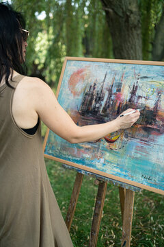Woman artist painter outdoor painting a canvas on an easel from behind, rear view
