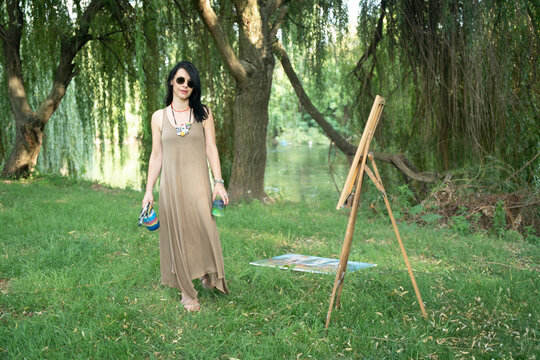 Portrait of a woman artist painter outoor painting by the river in sunglasses 