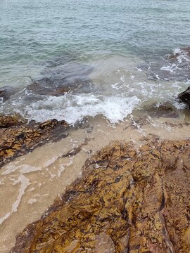 High angle view looking down at sea waves crashing against brown rocky shoreline with white foam splashing over stones.