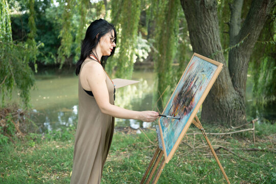 Beautiful woman painter by the river with sunglasses painting on a canvas on an easel