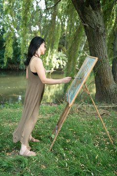Beautiful woman painter by the river with sunglasses painting on a canvas on an easel