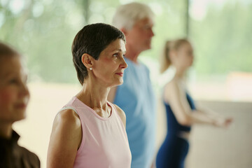 Fototapeta premium Mature Caucasian woman participating in group fitness class with senior man and young woman, promoting active lifestyle and wellness, medium shot