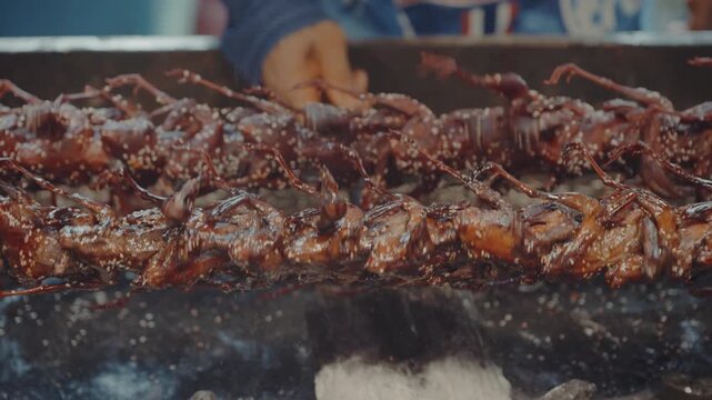 Close up of grilled quails turning on rotating spit at asian street food market