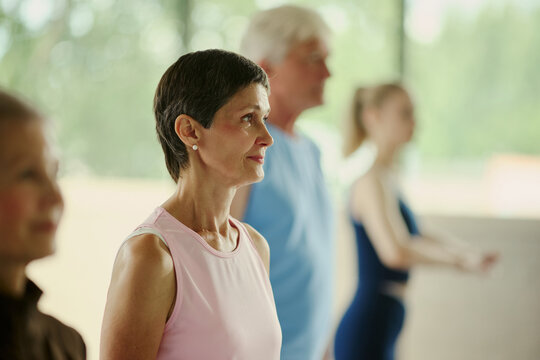 Mature Caucasian woman participating in group fitness class with senior man and young woman, promoting active lifestyle and wellness, medium shot