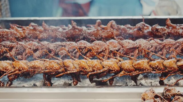 Close up of grilled quails turning on rotating spit at asian street food market