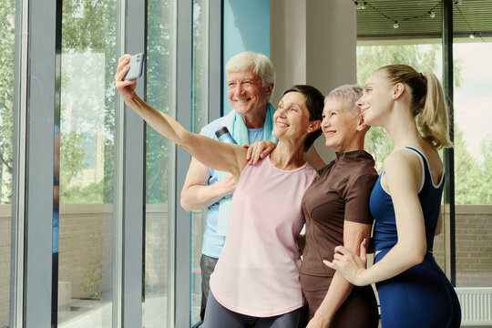 Diverse age group of Caucasian people taking selfie on smartphone in gym, smiling after workout. Image represents active lifestyle and is suitable for fitness marketing