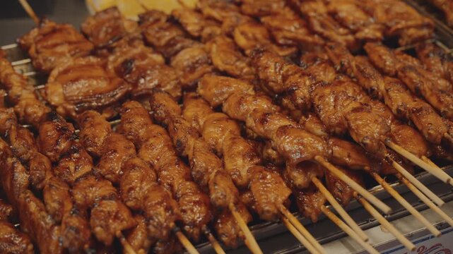 Traditional thai street food grilled chicken skewers with glistening sauce close up.