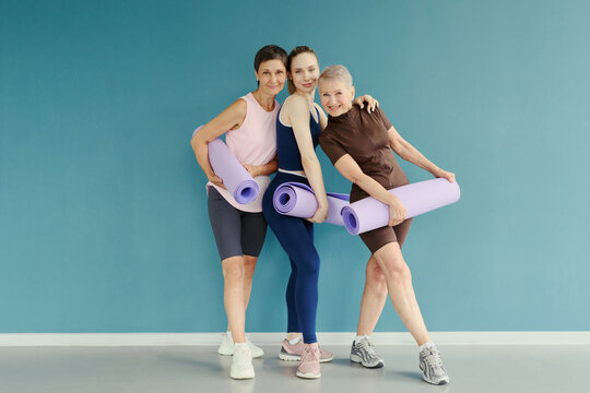Portrait of three Caucasian women of different generations holding yoga mats and smiling. Image represents active lifestyle and is suitable for fitness and wellness marketing campaigns