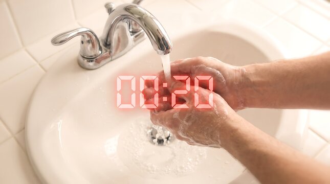Closeup of a person washing their hands with soap under a running faucet in a bathroom sink, with a digital timer overlay showing 20 seconds