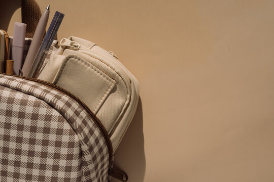 Checkered backpack with stationery and pencil case in warm light, back to school background.