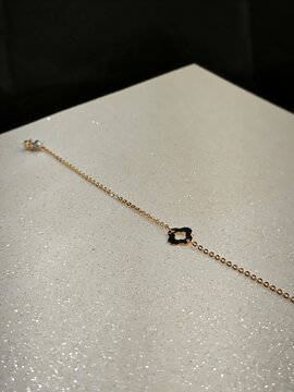 Delicate gold chain bracelet with clover charm and clasp. Minimalist jewelry on a sparkly white surface