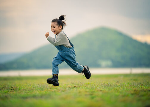 happy preschool child girl running on a grass field near river