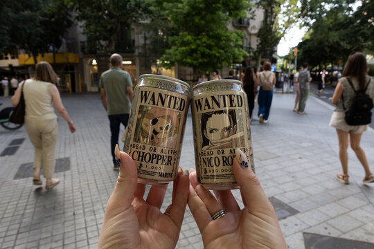 Barcelona, Spain - June 19, 2026: Hands holding One Piece beverage cans with Nico Robin and Tony Tony Chopper on a city street