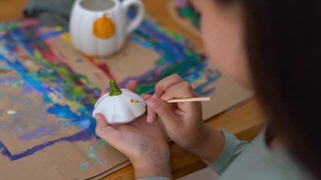 Young girl painting on a pumpking cup during fall season for Halloween event - Holiday, childhood and autumn lifestyle concept	