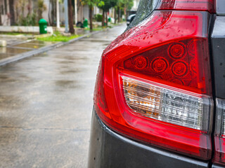 Wet Modern Car Taillight Detail. Close-up of a sleek red automobile rear light covered in fresh raindrops on a rainy street. © Robert Yap